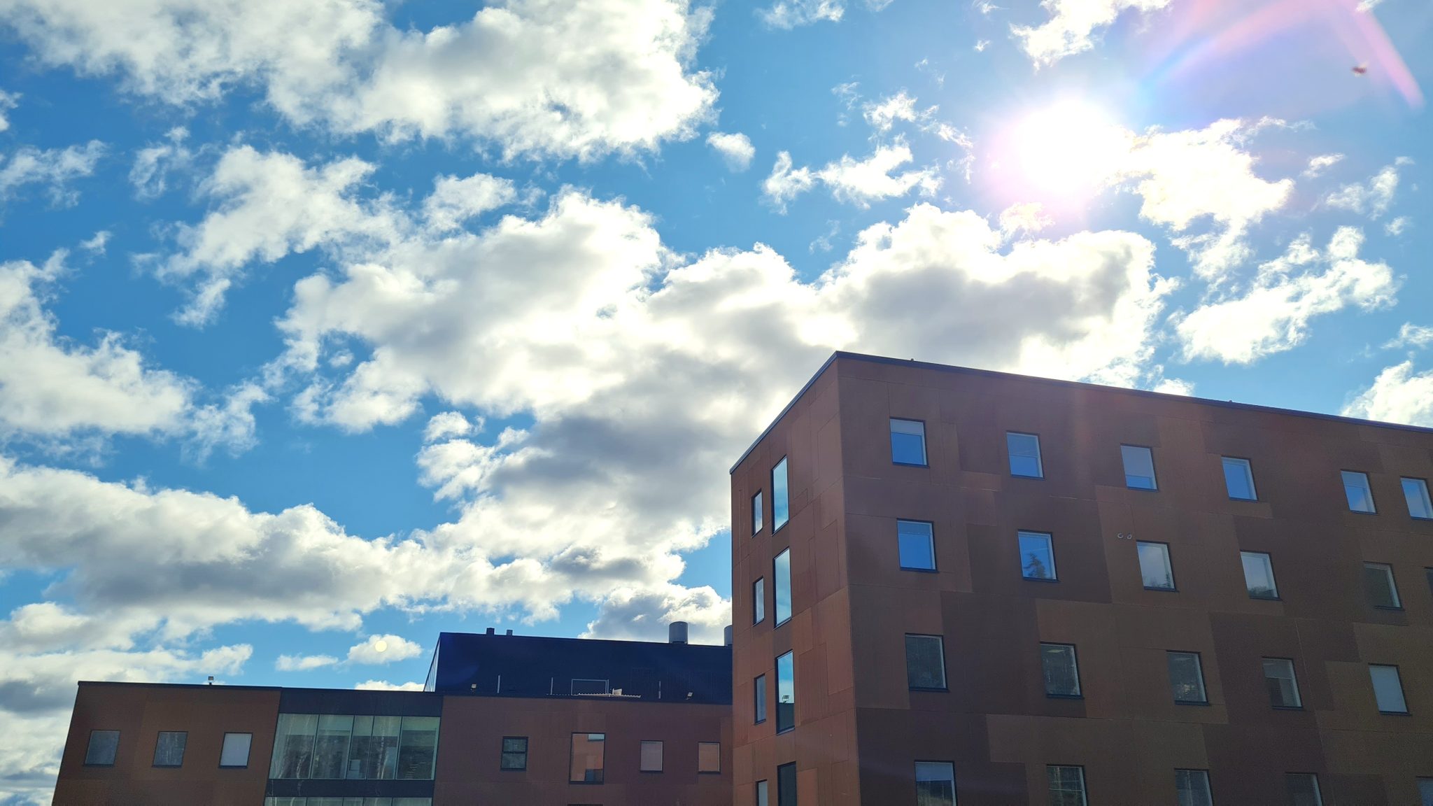 Hämeenlinnan uuden Ahveniston sairaalan ulkokuva. Kuvassa näkyy osio kahden rakennuksen yläkerroksista. Taustalla näkyy sininen taivas, jossa on satunnaisia pilviä.