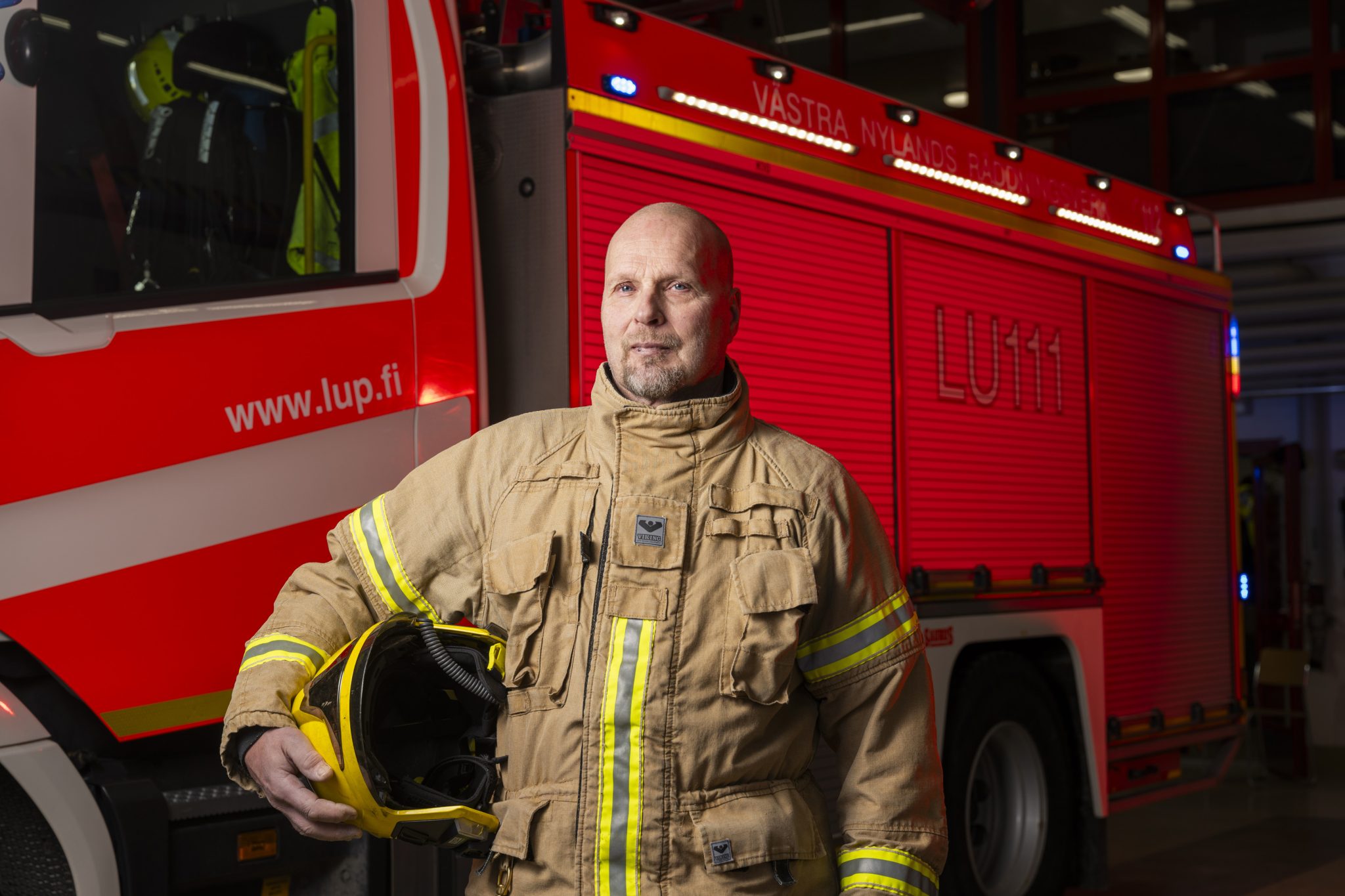 Palomies seisoo paloauton edessä hallissa ja katsoo kameraan