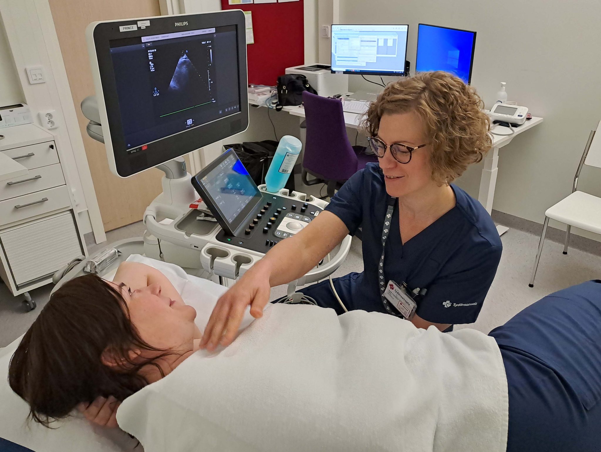 Sairaanhoitaja-sonograaferi peittelee vuoteella makaavaa potilasta sydämen ultraäänitutkimusta varten vastaanottohuoneessa